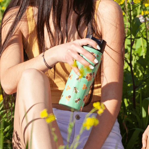 Woman holding a bee-themed reusable water bottle outdoors.