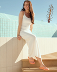 Woman in a white dress sitting on a ledge with a blue tiled wall and clear sky wearing orange flip flops