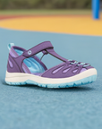 Kids Merrell Hydro Lily Fisherman Sandal on playground surface, highlighting its durable, water-friendly build and stylish purple-aqua color combo.