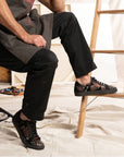 Man in black pants rests his foot on a ladder, wearing the Ander Rose sneakers.