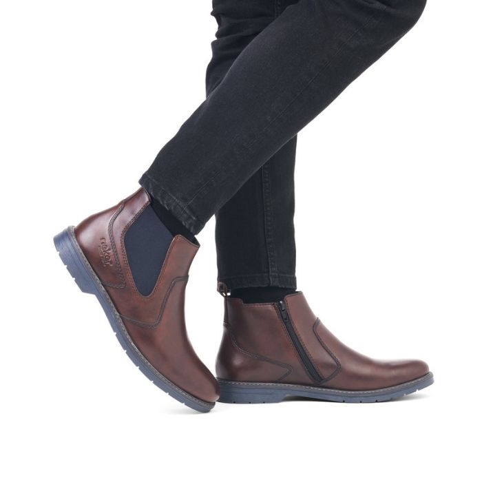 Legs in black jeans wearing brown leather Chelsea boot with navy elastic side goring.