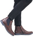 Legs in black jeans wearing brown leather Chelsea boot with navy elastic side goring.