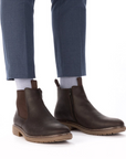 Brown leather chelsea boots worn with dusty blue dress pants and white socks.