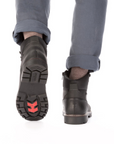 Black leather boots with red outsole grips worn with grey pants.