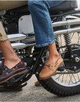 Two people sit on a motorcycle, wearing casual shoes with OrthoLite footbeds and jeans, highlighting footwear and bike details.