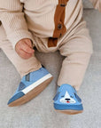 Baby sitting with blue dog canvas shoes on.