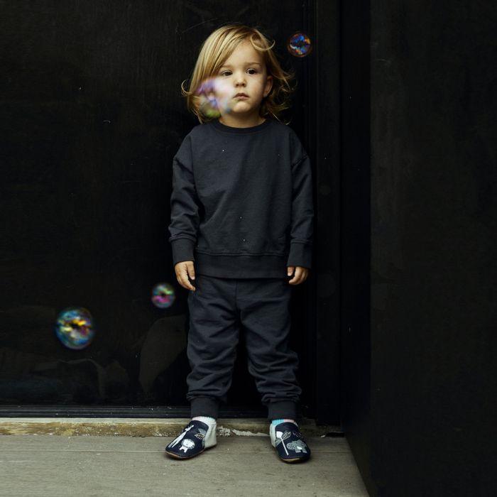 Toddler in black comfy clothes with bubbles floating around wearing the safari animal baby shoes