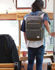 Man wearing gray Travelon Anti-Theft Heritage Backpack on public transport, showcasing its stylish design and travel-ready features.