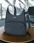 Travelon Anti-Theft Classic Messenger Bag in navy displayed on a table at an airport, showcasing its travel-ready design and anti-theft features.