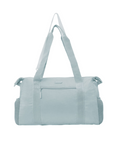 Light blue Travelon Pi Daily Carry Tote with minimalist design, front zipper pocket, and mesh side compartments for stylish, functional travel.