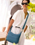 Woman wearing teal Travelon Anti-Theft Roam Medium Crossbody Bag outdoors, showcasing its stylish and secure design for travel.