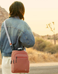 Person with a terracotta orange crossbody bag standing on a road in a desert landscape