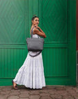 Woman carrying grey Travelon Anti-Theft Boho Tote in front of green door, showcasing stylish and secure handbag from Canadian Online Shoe Store.