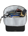 An open black zippered backpack with light grey interior lining filled with various travel accessories, including a pink watch, wallet, keys, and a rolled umbrella.
