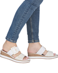 White slide wedge sandals with gold accents worn with blue jeans.