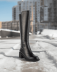 Women's Blondo Enza heeled boot standing on snowy pavement, showcasing waterproof leather and durable sole for cold-weather fashion.