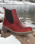 Red Bos&Co Corra Chelsea winter boot for women displayed outdoors on snowy rocks, showcasing waterproof leather and cold-rated wool lining.