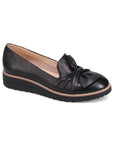 A black leather loafer with a scrunchy bow detail on the vamp and a low wedge heel.