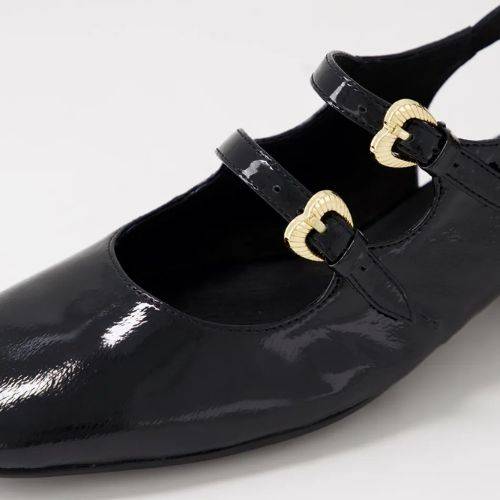 Close-up of black Django & Juliette Viraz Slingback Heels showing glossy leather and heart-shaped gold buckle strap details.