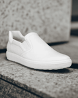 Women's Ecco Soft 7W Slip-On Sneaker displayed outdoors on stone surface, highlighting sleek white leather and minimalist slip-on design.