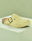 Light green El Naturalista clog displayed on a minimalist green pedestal, showcasing its suede finish and buckle detail.
