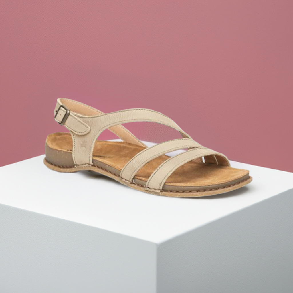 Women's Backstrap Leather Sandal in brown 3 thin cross straps, buckled ankle strap and thin beige footbed with tan rubber outsole on a white block and pink background.