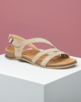 Women's Backstrap Leather Sandal in brown 3 thin cross straps, buckled ankle strap and thin beige footbed with tan rubber outsole on a white block and pink background.