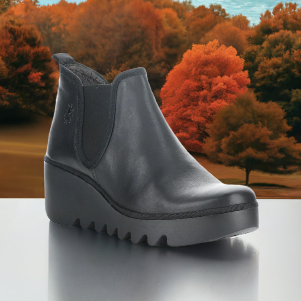 Women's FLY London Byne Wedge Boot in black leather displayed against a fall foliage background, ideal for autumn fashion and comfort.