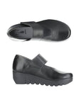 Pair of black Mary-Jane style shoes with a Velcro strap, Fly London logo on grey footbed and a thick lugged rubber sole.