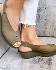 Model wearing olive green FLY London Yeay Wedge Sandals styled with white jeans, highlighting comfort and modern design.