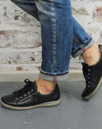 Model wearing jeans walking in the Caren 12 Sneakers in black.