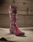 L'Artiste Rodeoqueen Western Boot displayed in rustic setting, highlighting red leather, floral print, and 2-inch heel for women.