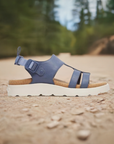 Women's Merrell Fleur Backstrap Sandal in navy blue shown outdoors on a trail, highlighting its rugged sole and stylish design for active lifestyles.