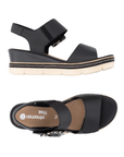 Pair of Black backstrap platform sandals with oversized decorative buckle, two Velcro straps, tan Remonte logo'd footbed, a faux wood grain wedge midsole and an off-white outsole.