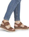 Brown wedge sandals with decorative square buckle worn with blue jeans.