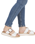 White sandals with a decorative buckle worn with blue jeans.