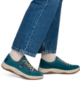A person wearing blue jeans, white socks, and teal low-top sneakers with beige laces and a side zipper.