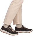 A person wearing beige pants and dark brown low-top sneakers with beige laces and outsole.