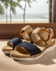 Backstrap Sandals in tan and navy displayed in a tropical cottage scene.