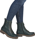 Green leather combat boots with brown soles worn with blue jeans.