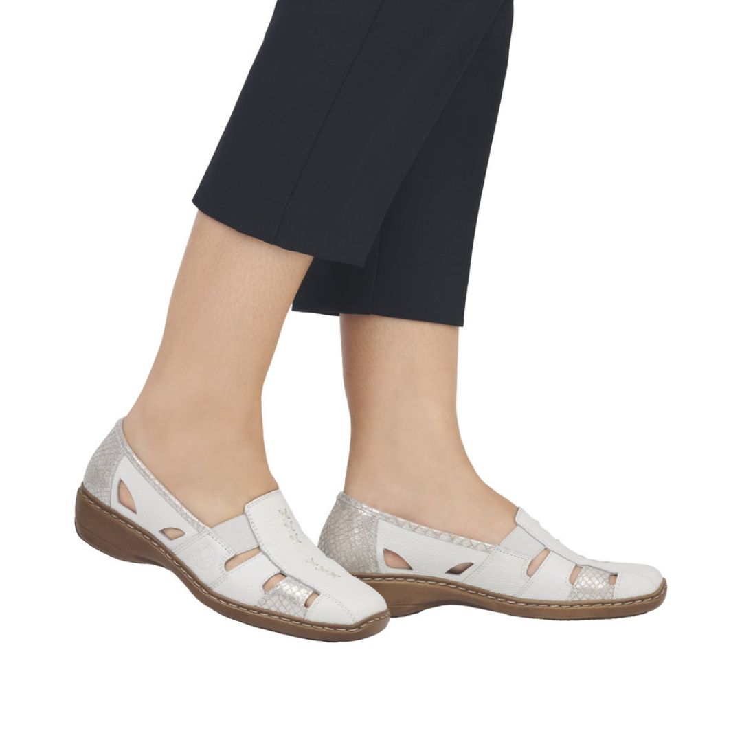 Model wearing white leather loafers with cutouts and black pants.