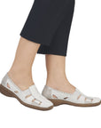 Model wearing white leather loafers with cutouts and black pants.