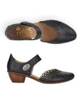 Pair of black heeled open sided Mary-Janes with Velcro ankle strap, floral pattern, decorative perforations and a low stacked heel.