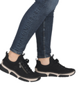 Black sneakers with beige midsole worn with blue jeans.