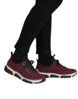 Deep red sneaker with faux side zipper, accent stitching above the thick beige midsole and black outsole worn with black pants.