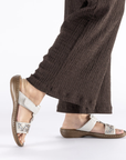 Woman wearing brown pants and silver slide sandals with decorative bead design.