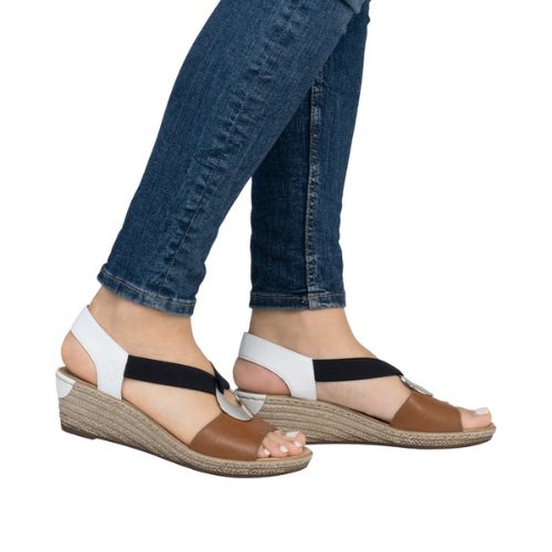 Model wearing brown and white Rieker 624H6 Sling-Back Wedge Sandals with jeans. Stylish and comfortable for everyday fashion.
