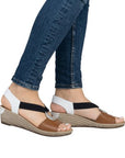 Model wearing brown and white Rieker 624H6 Sling-Back Wedge Sandals with jeans. Stylish and comfortable for everyday fashion.