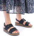Model wearing black Women's Rieker 62950 Backstrap Sandals paired with a patterned skirt, highlighting the sandal's casual elegance.
