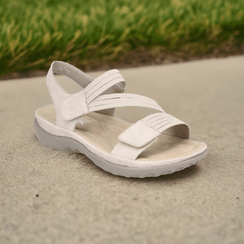 Beige Women's Rieker 64870 Backstrap Sandal displayed outdoors on pavement, highlighting its casual style and comfort fit.